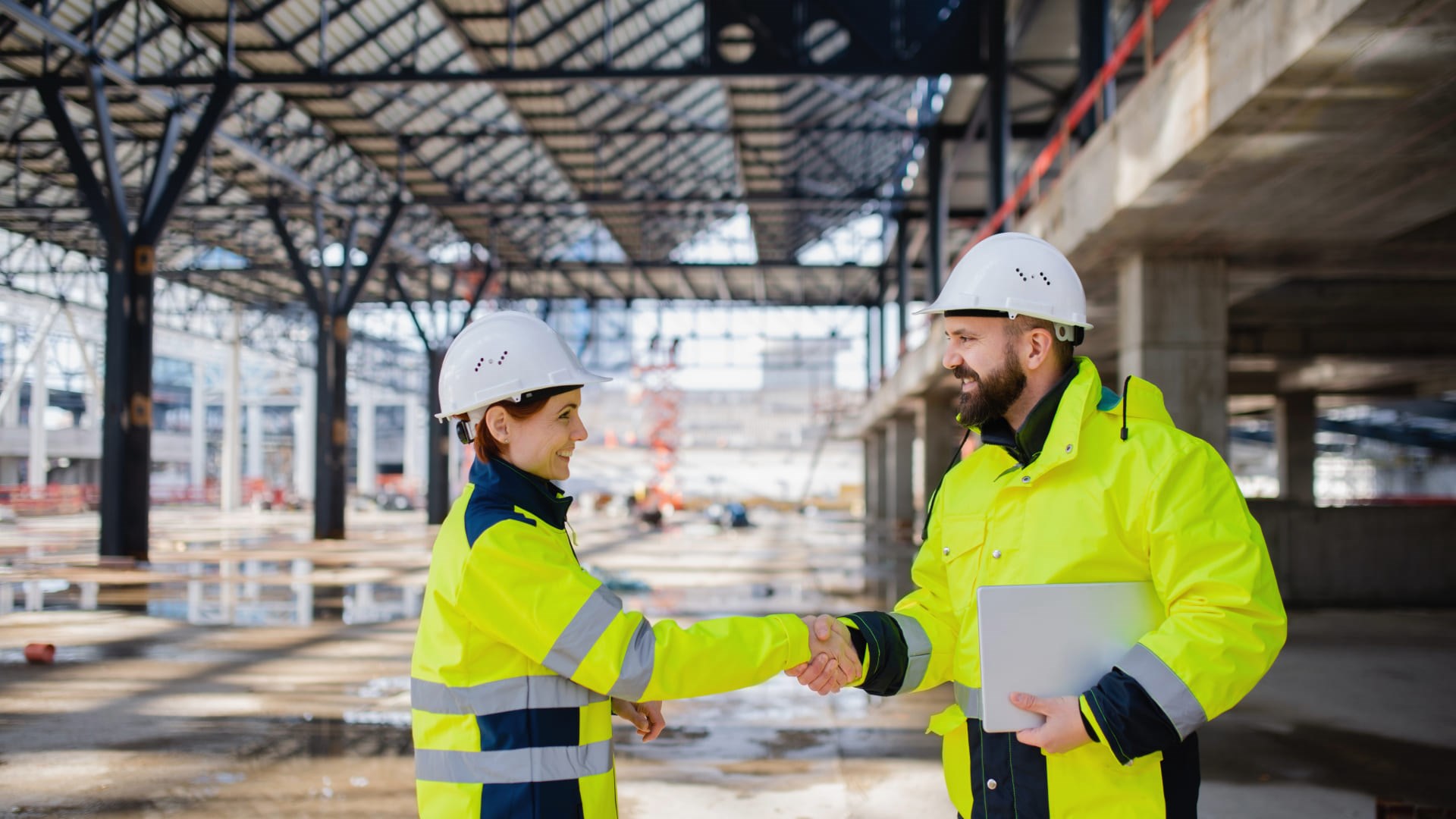 Deux professionnels en équipement de sécurité se serrent la main sur un chantier, symbole de collaboration et de service client personnalisé.